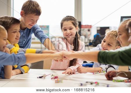 education, children, technology, science and people concept - group of happy kids building robots at robotics lesson and making fist bump