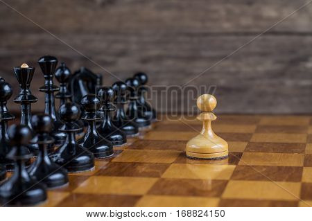 One pawn staying against full set of black chess pieces. With selective focus on pawn.