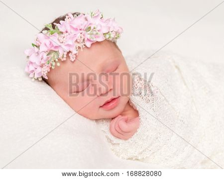 cute newborn baby in headband with flowers smiling asleep, closeup