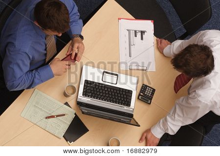 两个商人在讨论中，看着笔记本电脑，文书工作 ；从上面射击了。