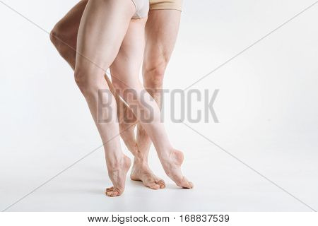 Elegant ballet dancers legs . Gracile elegant athletic ballet dancers legs located in the white colored studio and demonstrating dancing pa