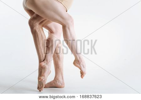 Professionalism in details. Tensed sinewy muscular ballet dancers legs located in the white studio and being tensed while standing on the white floor