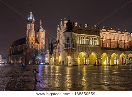 Main Market Square - Rynek Glowny - with Sukiennice - Cloth Hall - and St. Mary's - Mariacki - Churche with reflection in wet pavement at night Poland Krakow