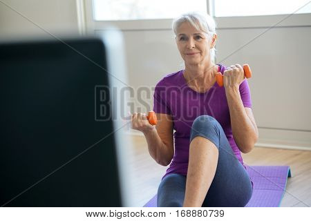 Senior woman doing fitness exercices in front of tv