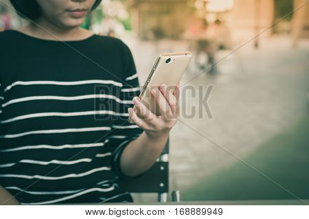 Weekend activity scene of adult Asian woman watiching on mobile phone at coffee shop with vintage filter effect. Urban lifestyle with technology concept.