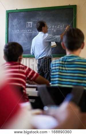 Young people and education. Group of hispanic students in class at school during lesson. Focus on teacher at blackboard explaining math.