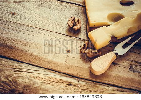 Maasdam cheese with walnuts on a dark cutting board top right angle with cheese fork, selective focus, toned