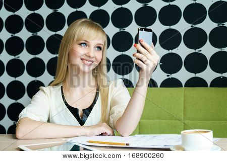 Blonde girl sitting in cafe holds a mobile phone