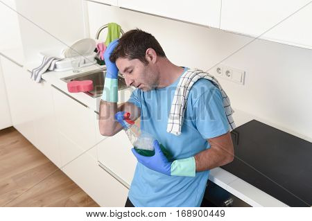 young lazy house cleaner man washing and cleaning the kitchen with detergent spray bottle and sponge in stress and desperate face expression in male housework and housekeeping concept