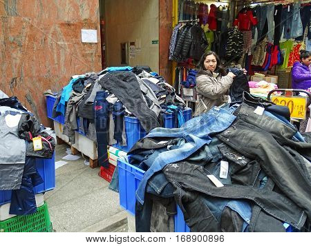 North Point, Hong Kong - February 10, 2016: A woman is standing at an big heap of jeans and other pants at a street market in North Point, Hong Kong. The selling price is displayed on large price tags.