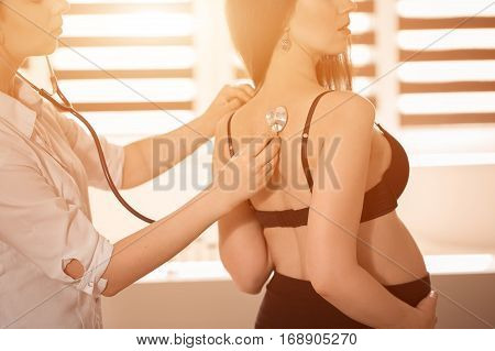 Friendly Female Medicine Doctor Holding Stethoscope And Listening To Pregnant Woman Standing For Enc