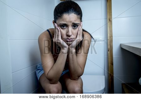 young sad and depressed bulimic woman feeling sick sitting in toilet WC looking desperate and ill in pregnancy and depression concept
