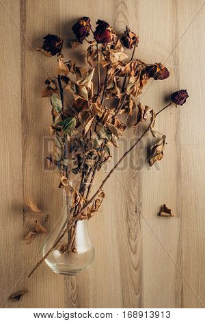 Bouquet of dried and wilted roses in the glass vase lying on wooden floor.