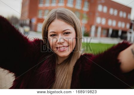 Pretty blonde girl with fur coat in the park making herself a photo