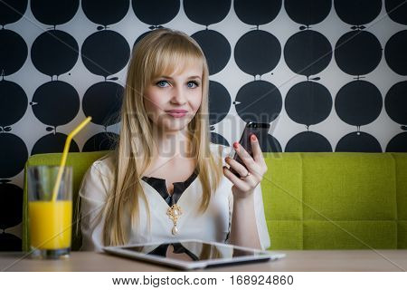 Young girl texting sms using a mobile phone and drinking orange juice at the cafe