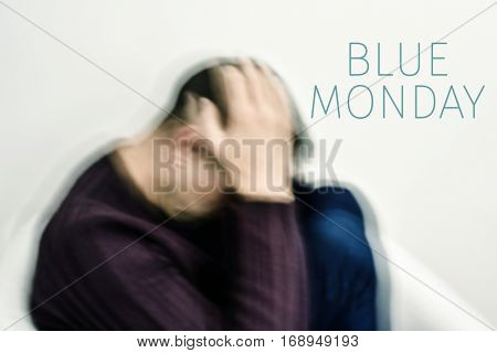 closeup of a blurred young caucasian man curled up with his hands in his head and the text blue monday