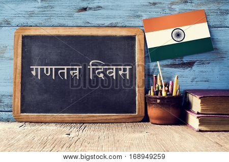 a chalkboard with the text Republic Day written in Hindi and a flag of India, on a rustic wooden surface, against a blue wooden background