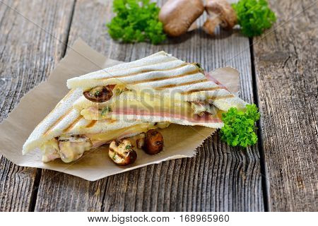 Pressed and toasted double panini with ham, cheese and mushrooms served on sandwich paper on a wooden table