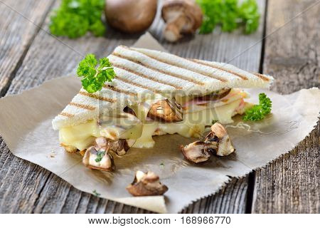 Pressed and toasted double panini with ham, cheese and mushrooms served on sandwich paper on a wooden table