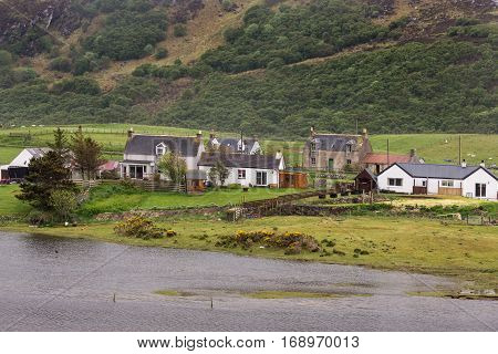North Coast Scotland - June 6 2012: A handful of houses stand together along the Naver River on a green landscape with the of a rough brown and dark green mountain just behind them. Houses add whites and reds.