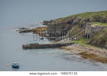 North Coast Scotland - June 6 2012: A short and narrow stone dock protrudes into Loch Eriboll. Brown green cliffs a small fishing boat and plenty of bluish gray water.