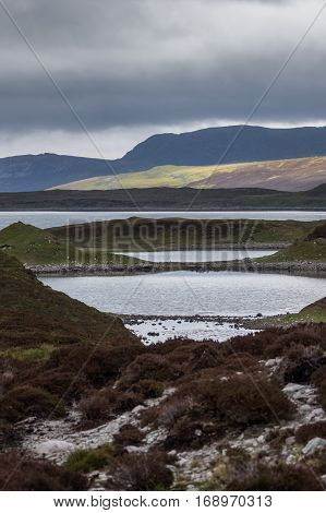 North Coast, Scotland - June 6, 2012: Irregularly shaped gray-water Loch Eriboll under dark cloudy skies. Wide shot showing land tongues background mountains and green and brown vegetation.
