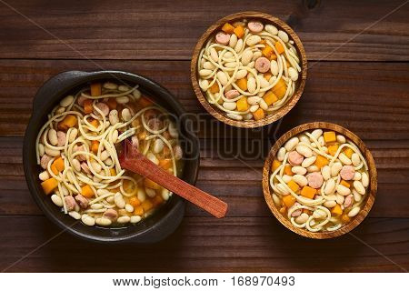 Chilean traditional Porotos con Riendas (beans with reins) dish of cooked dried beans with pumpkin onion spaghetti and sausage in rustic bowls photographed overhead on dark wood with natural light