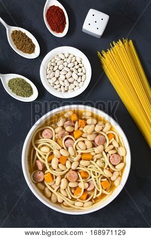 Chilean traditional Porotos con Riendas (beans with reins) dish of cooked dried beans with pumpkin onion spaghetti sausage with ingredients on the side (cumin paprika oregano white dried beans spaghetti) on the side photographed overhead on slate with nat