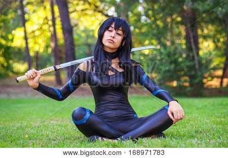 Young girl closed eyes sitting on the grass and holding samurai sword. Original cosplay character