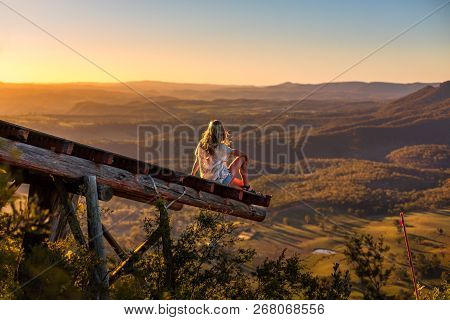 Female In Casual Clothes With Sunlit Hair Flowing In The Breeze Relaxes On The Timber Platform That 