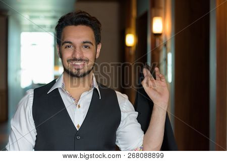 Young Happy Indian Man Smiling While Holding Jacket In The Corri
