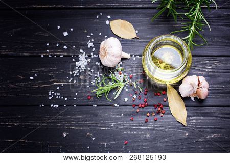Bottle With Olive Oil With Herb And Spices Ob Black Wooden Background. Selective Focus. Place For Te