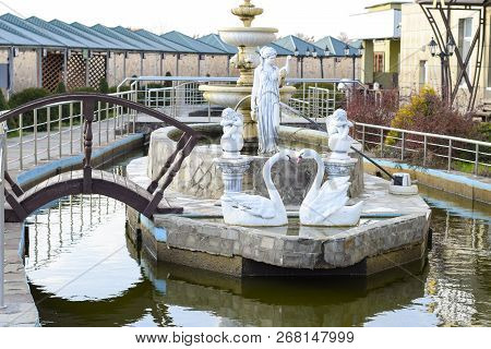 Sculptures Of A City Fountain At A Street Cafe. Gypsum Swans And Female Figures