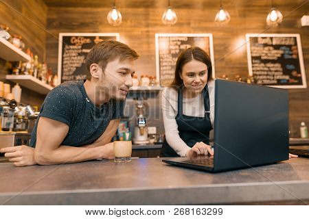 Young Couple Man And Woman Owners Of Small Modern Coffee House Using Laptop Computer For Work.