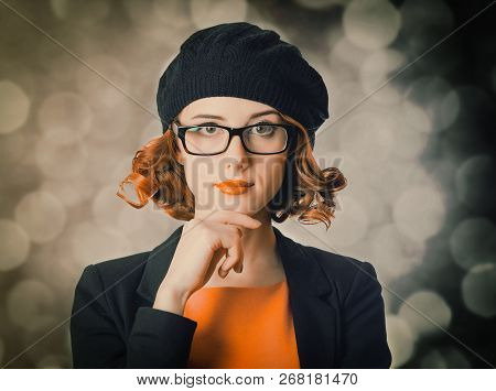 Portrait Of A Beautiful Girl With Curly Hair Dressed In A Beret And Jacket Against A Gray Background