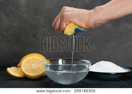 Woman Squeezing Out Sponge Over Bowl With Water And Baking Soda On Dark Table