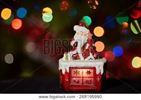 Santa Claus Statuette Doing An Exercise Waiting For Christmas. Colored Bokeh