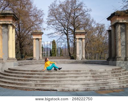 Smiling Enjoying Girl Sitting On The Staircase Of The Round Area With Columns, Looking At The Spring