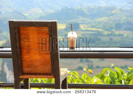 A Back Of Wood Seating Chair And Iced Coffee Cup With Natural Green View.