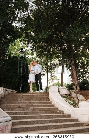 Beautiful Cuple Stand On The Stairs And Hug Each Other. Man And Woman Walking In The Park. Lovestory