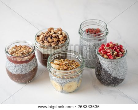 Set Of Chia Pudding In Different Glass Jars On White Marble. Assortment Of Chia Puding With Differen