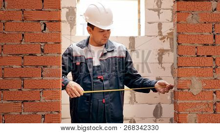 Man Working On Site Of Building House And Measuring Width Of Doorway In Brick Wall With Tape