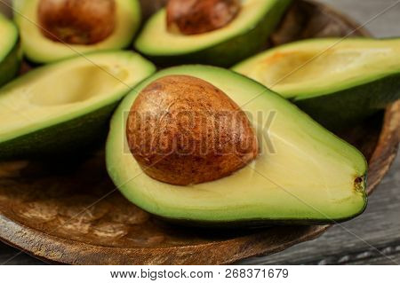 Close Up Photo Of Avocado Halves On Wooden Carved Bowl, Detail On The Brown Seed / Pit.