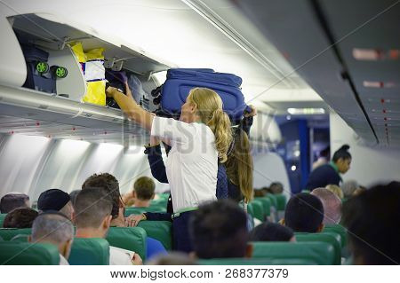 The Stewardess Helps The Passengers To Put Their Luggage In The Cabin Of The Plane. Stewardess In Th