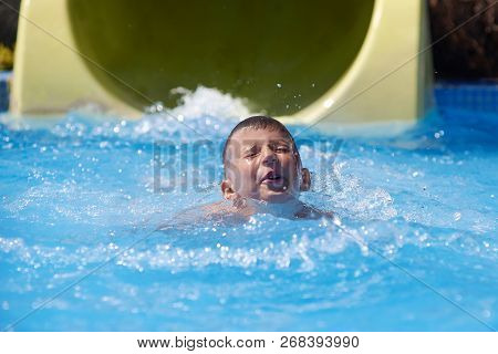 Caucasian Boy Swimming In Waterpark Pool After Diving From Gliding Flume.