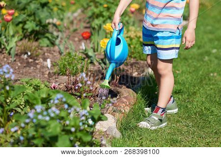 Boy With Blue Watering Can In His Hands Helping To Water The Flowers In A Countryside Croft.
