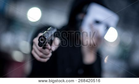 Mystery Hoodie Man In White Mask Pointing Gun. Crime And Violence Concepts. Focus On Gun