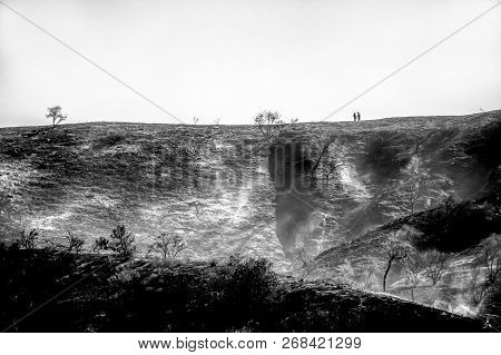 Couple Walks Along Ridge Over Burned Landscape In Black And White Image Of California Woolsey Fire.