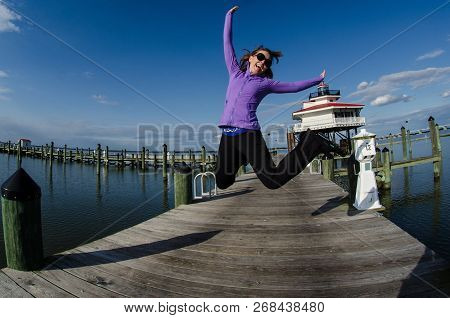 Beautiful Woman Jumps On A Dock Alongside The Choptank River Lighthouse In Maryland