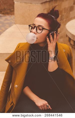 Cute Young Girl Listening To Music On Headphones In Autumn Park. Girl Has Eggplant Hair. Woman Blew 